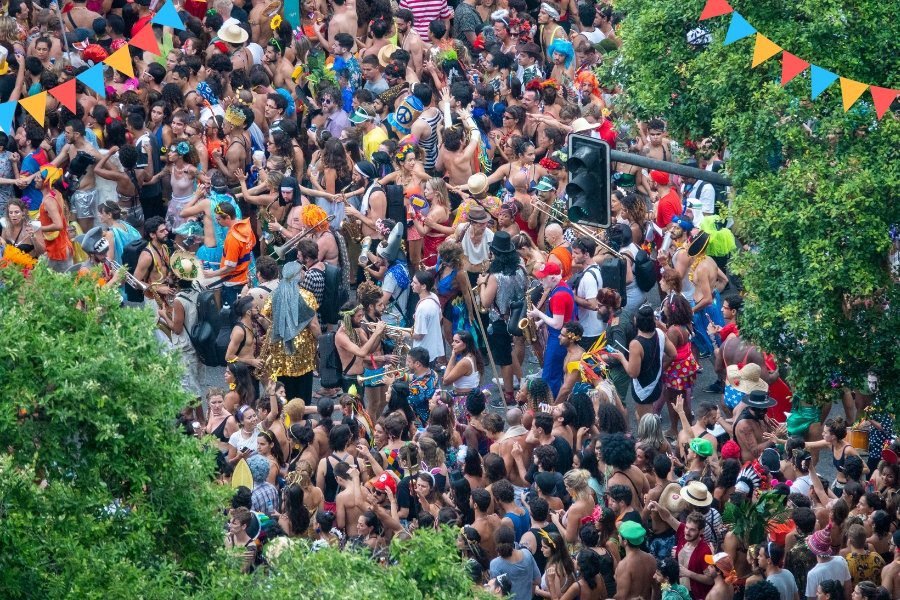 Foliões animados em um bloco de rua durante o Carnaval, vestindo fantasias coloridas e dançando ao som de marchinhas e samba em uma atmosfera festiva.